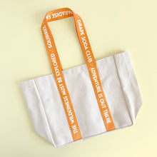 Load image into Gallery viewer, White tote bag with orange handles featuring text on a light yellow background