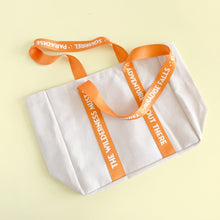 Load image into Gallery viewer, White tote bag with orange handles and text on a light yellow background