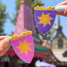 Load image into Gallery viewer, Two pennant flags with a sun design, one purple and one pink, held against a princess background of colorful architecture.