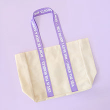 Load image into Gallery viewer, Beige canvas tote bag with purple handles featuring Ariel Little Mermaid quotes on a light purple background
