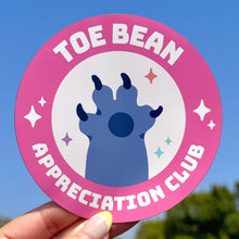 Load image into Gallery viewer, Sticker with &#39;Toe Bean Appreciation Club&#39; design held against a blue sky.
