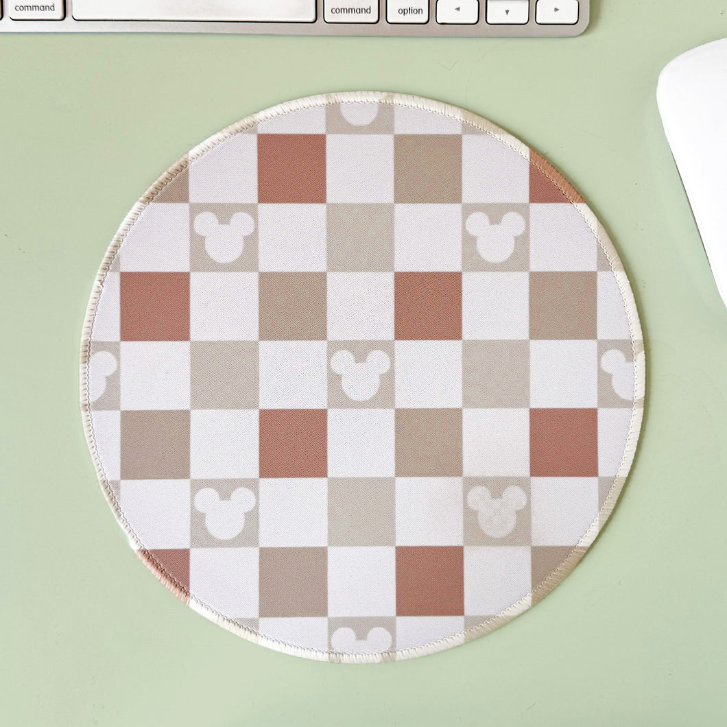 Round checkered mouse pad with Mouse icons on a light green surface with a keyboard and mouse.