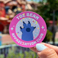 Load image into Gallery viewer, Sticker with &#39;Toe Bean Appreciation Club&#39; design held by a hand outdoors.
