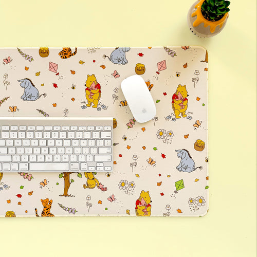 Desk setup with a Winnie the Pooh-themed desk mat, keyboard, and mouse on a yellow background.